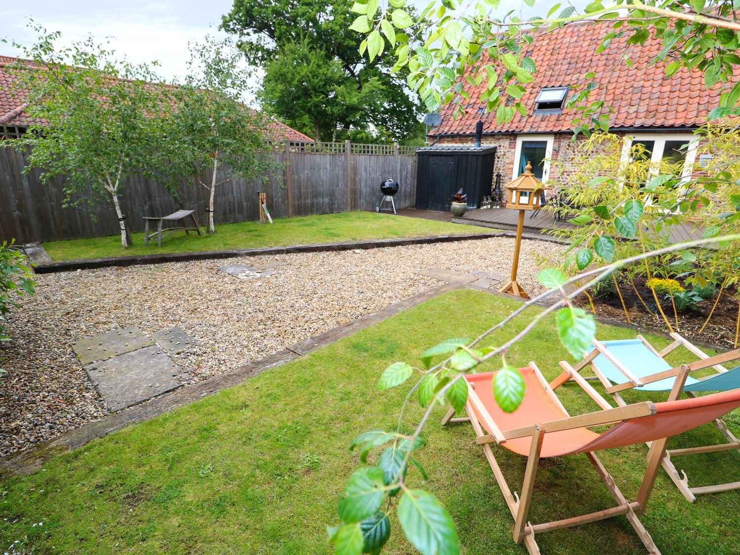 Ein Garten mit Kiesfläche, Holzzaun, kleiner Gartenhütte und einem Vogelhäuschen.