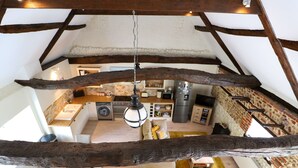 Ein Dachzimmer mit freiliegenden Holzbalken, einer Küchenzeile mit modernen Geräten und einer gemütlichen Sitzecke mit Kissen.