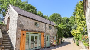 A stone building with a wooden door and a small porch with a bench. - The Old Coach House (Mold)