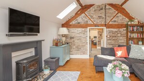 A cozy living room with a fireplace, a sofa, a coffee table with flowers, a bookshelf, and a TV mounted on the wall. - The Old Coach House (Mold)