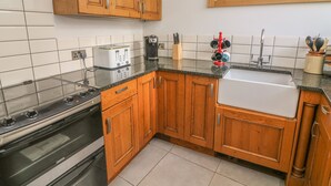 A kitchen with wooden cabinets, a stove, a toaster, a coffee maker, and a sink. - Flat 2 Galloway House (Kendal)