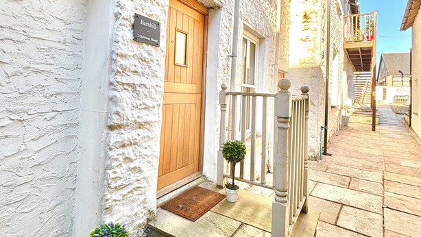 A narrow street with a white building featuring a wooden door and a small porch with a potted plant. - Flat 2 Galloway House (Kendal)