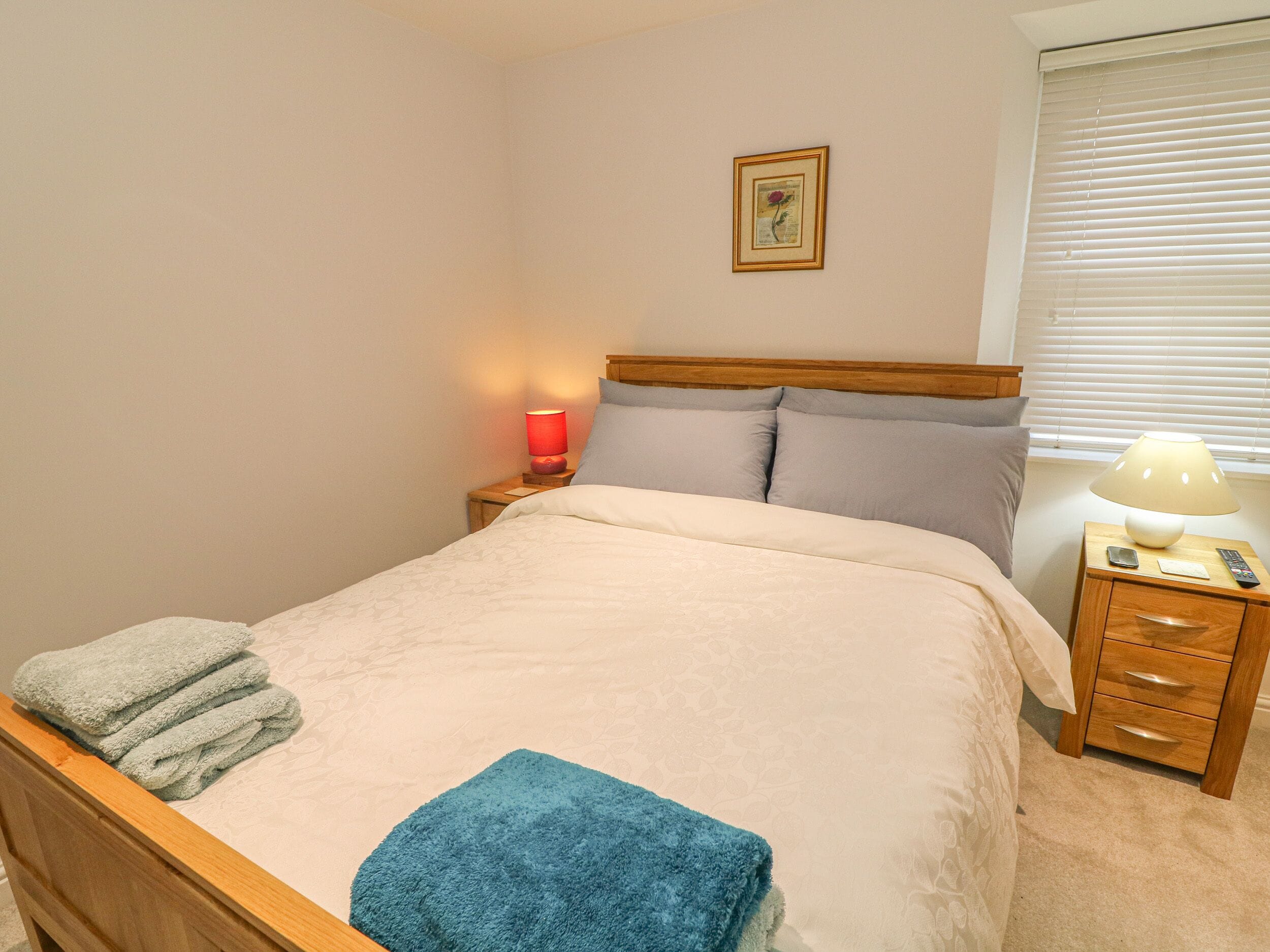 A neatly made bed with a blue towel, a red lamp on the nightstand, and a framed picture on the wall.