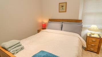 A neatly made bed with a blue towel, a red lamp on the nightstand, and a framed picture on the wall.