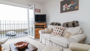 A living room with a sofa, a coffee table, a TV, and a painting on the wall. - 14 Lyme Mews (Seaton)