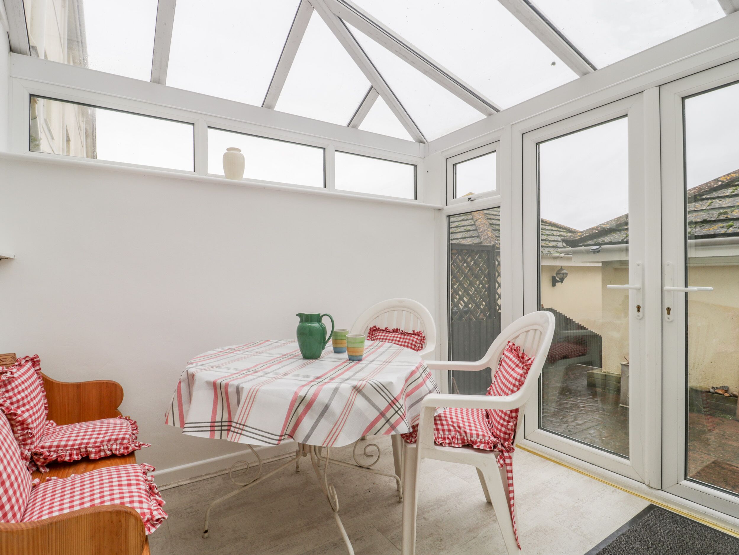 A conservatory with a table and chairs, a green pitcher, and a checkered tablecloth.
