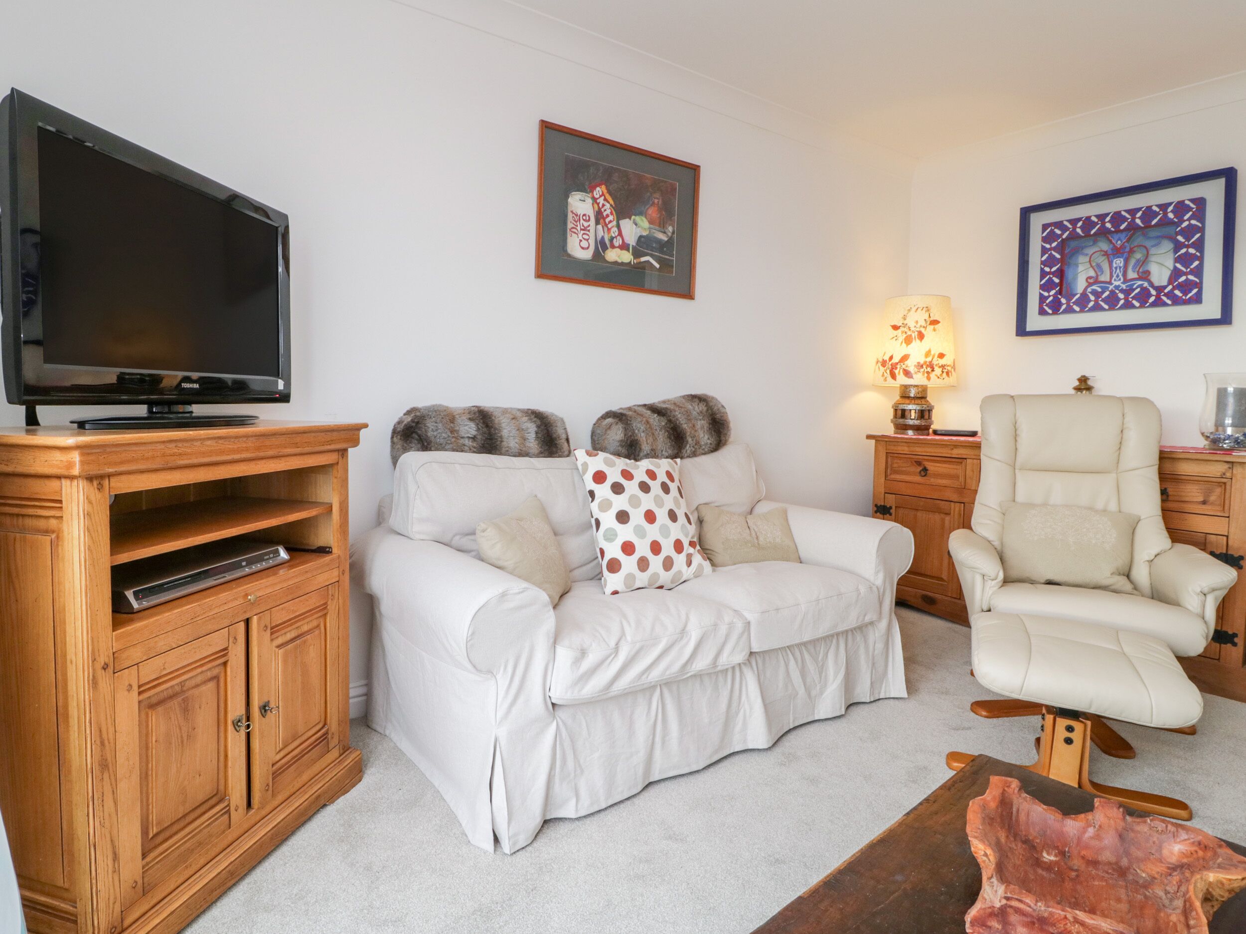 A living room with a flat-screen TV, a sofa, a chair, wooden cabinets, and a framed picture on the wall.