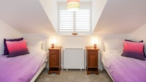 A bedroom with two beds, a window with blinds, a radiator, and a ceiling light fixture. - 14 Lyme Mews (Seaton)