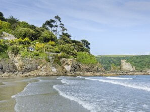 A coastal landscape with a rocky shoreline, waves, and lush greenery.