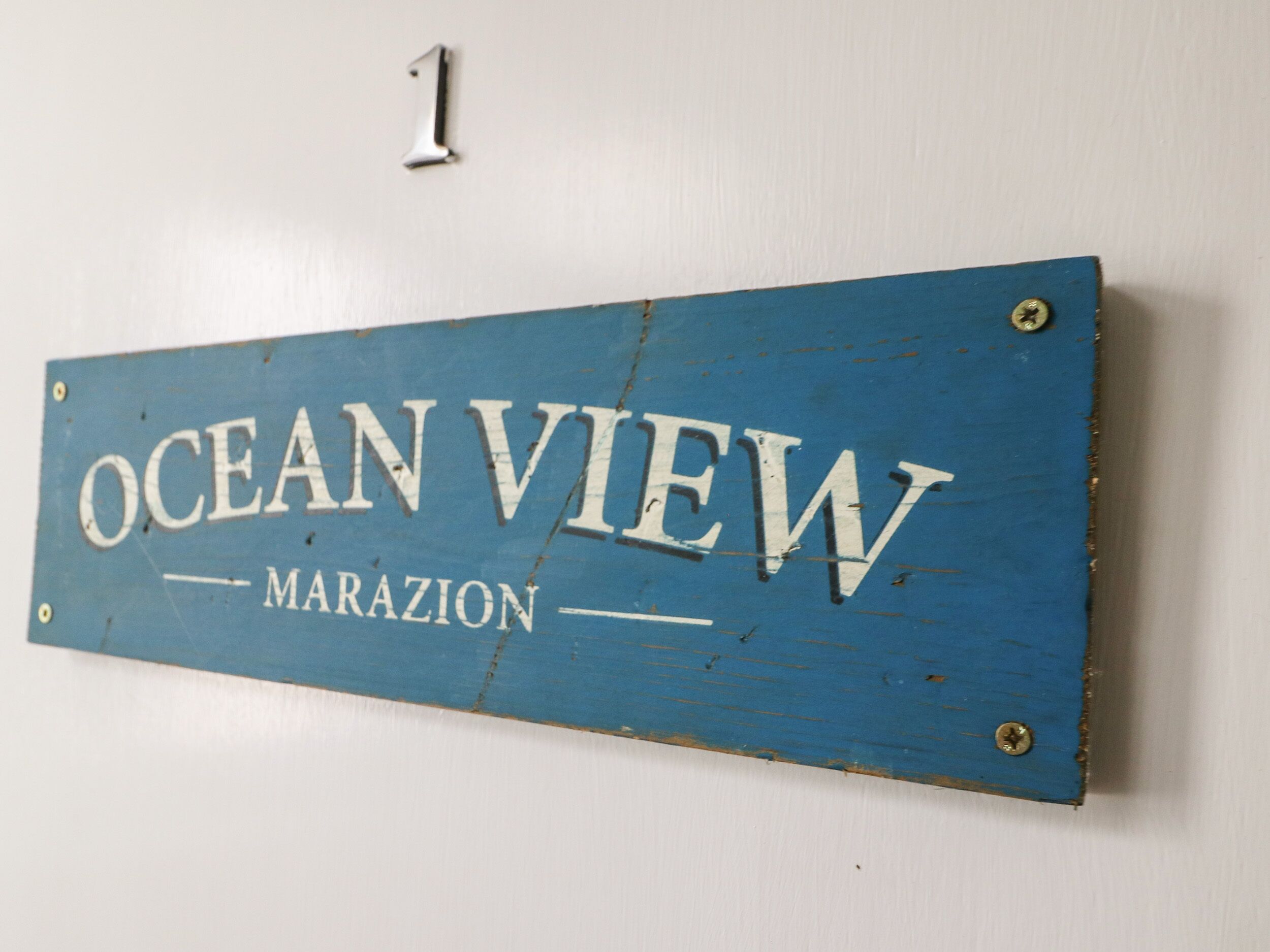 A blue sign with the text "OCEAN VIEW MARAZION" mounted on a white wall.