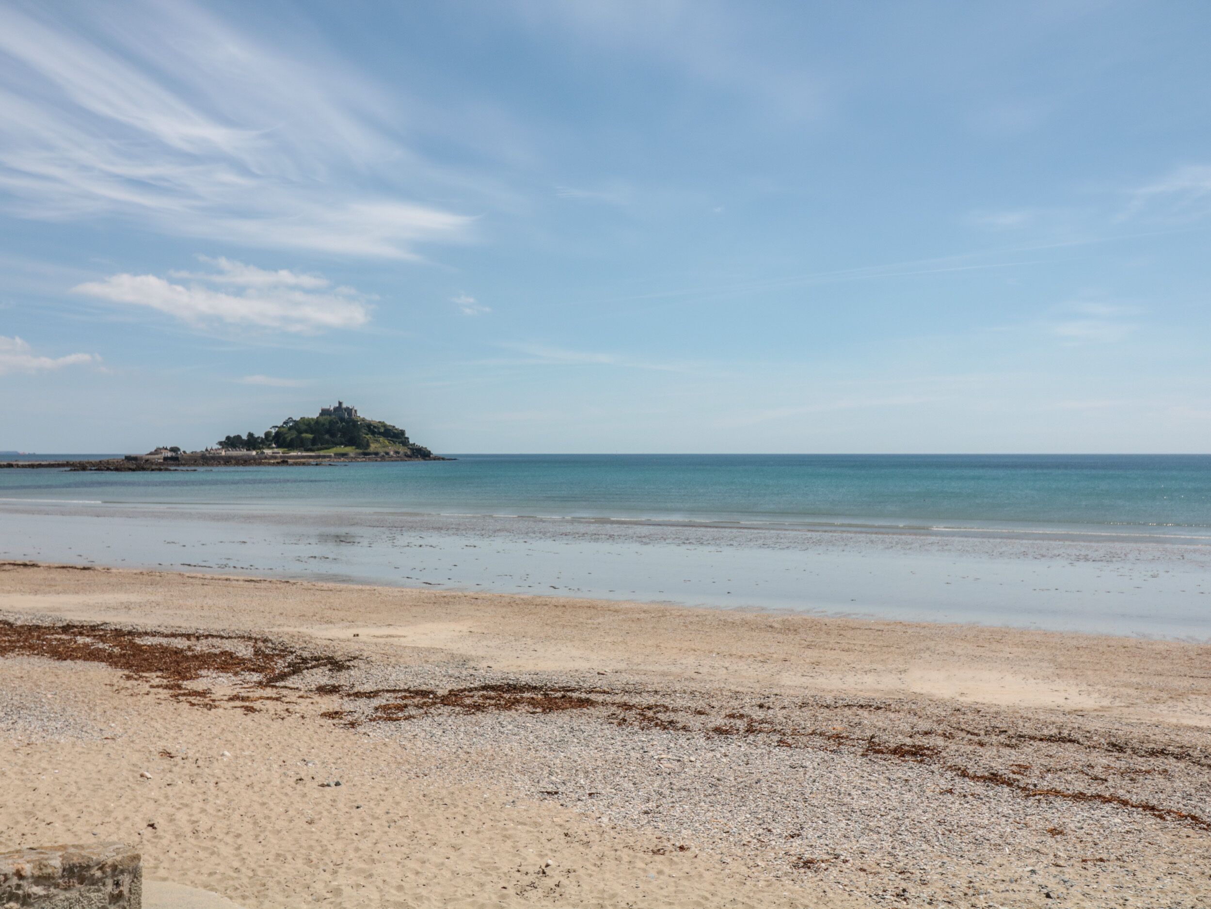 A beach with a pebbly shore and a distant island with buildings.