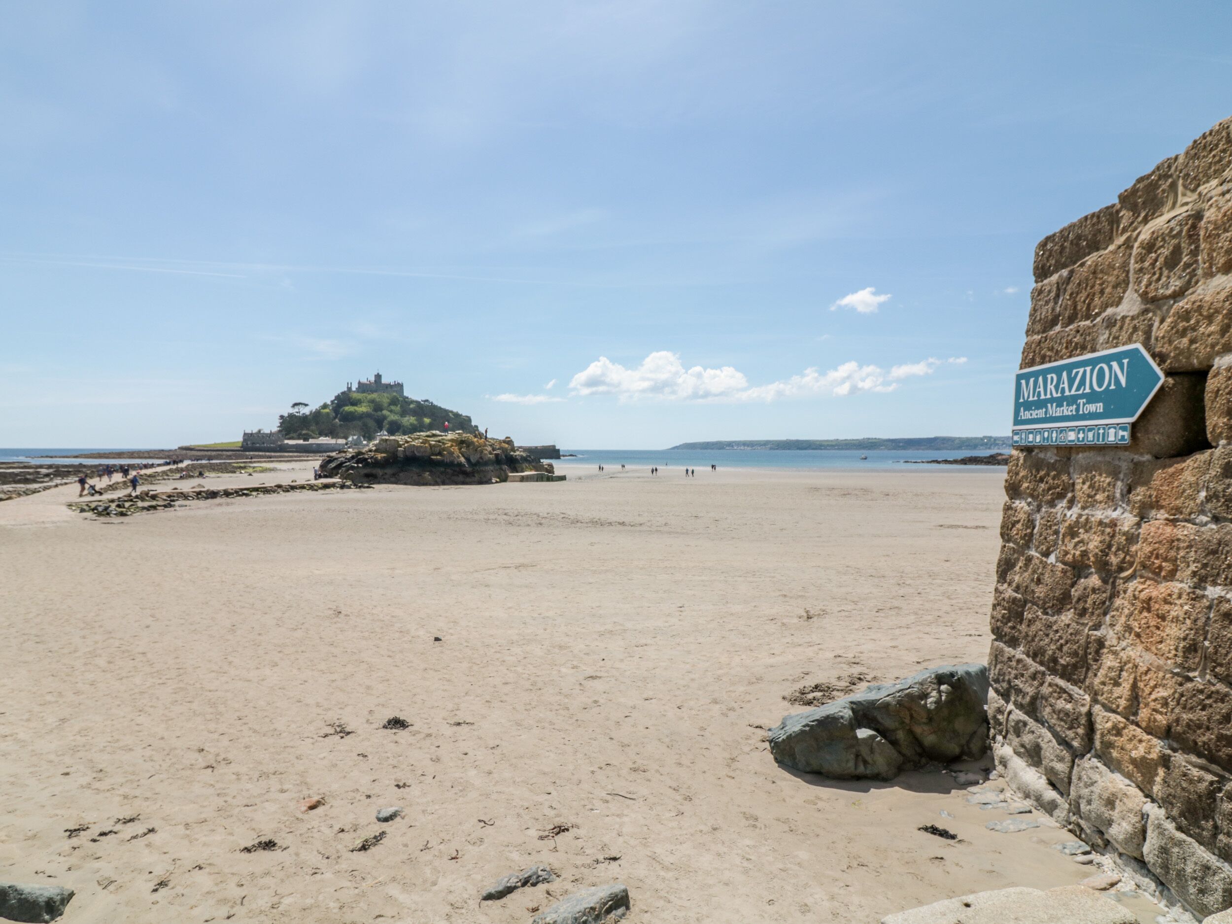 A beach with a stone wall and a sign reading "MARAZION Ancient Market Town".