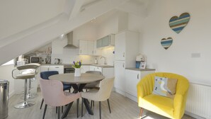 Una cocina moderna con armarios blancos, una mesa de comedor con sillas, un sillón amarillo y decoración con arte mural en forma de corazón.