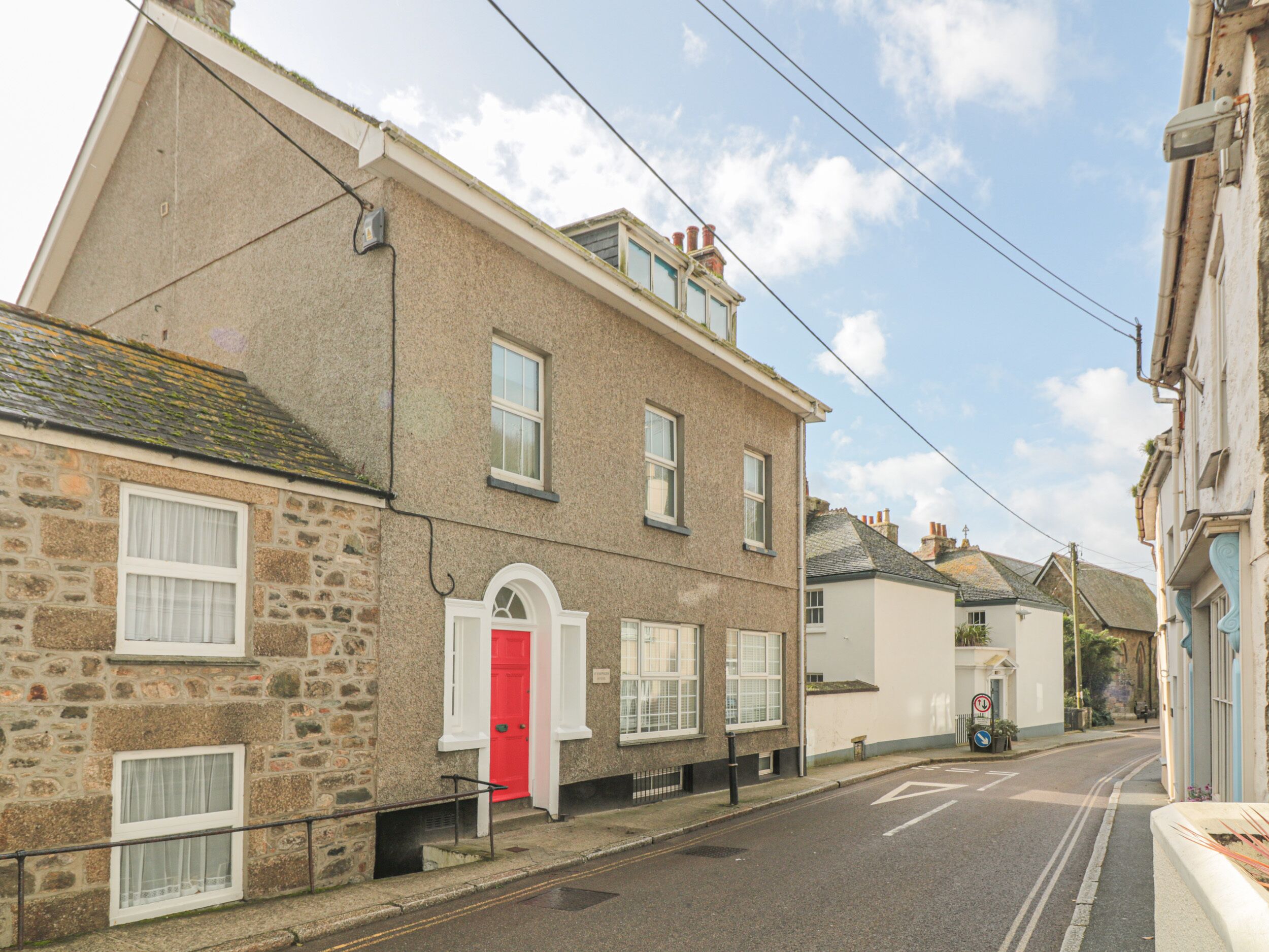 A street view with a two-story stone building featuring a red door and multiple windows.