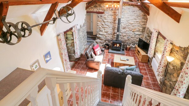 A cozy interior with a stone fireplace, wooden beams, and a staircase. - Melin Bach (Garndolbenmaen)