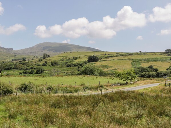 A rural landscape with rolling hills, a winding road, and sparse vegetation. - Melin Bach (Garndolbenmaen)