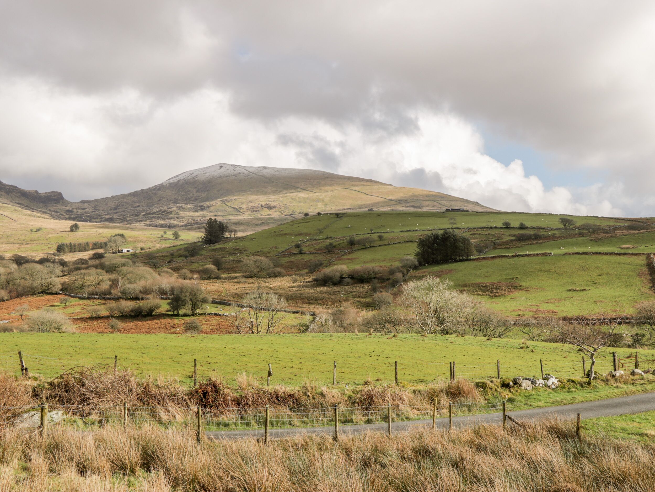 A rural landscape with rolling hills, a road, and a fence.
