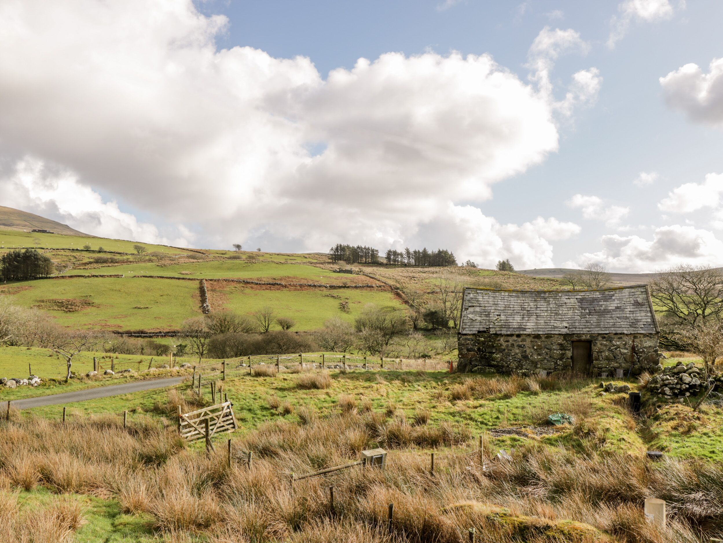 A rural landscape with a stone building, a road, and rolling hills.