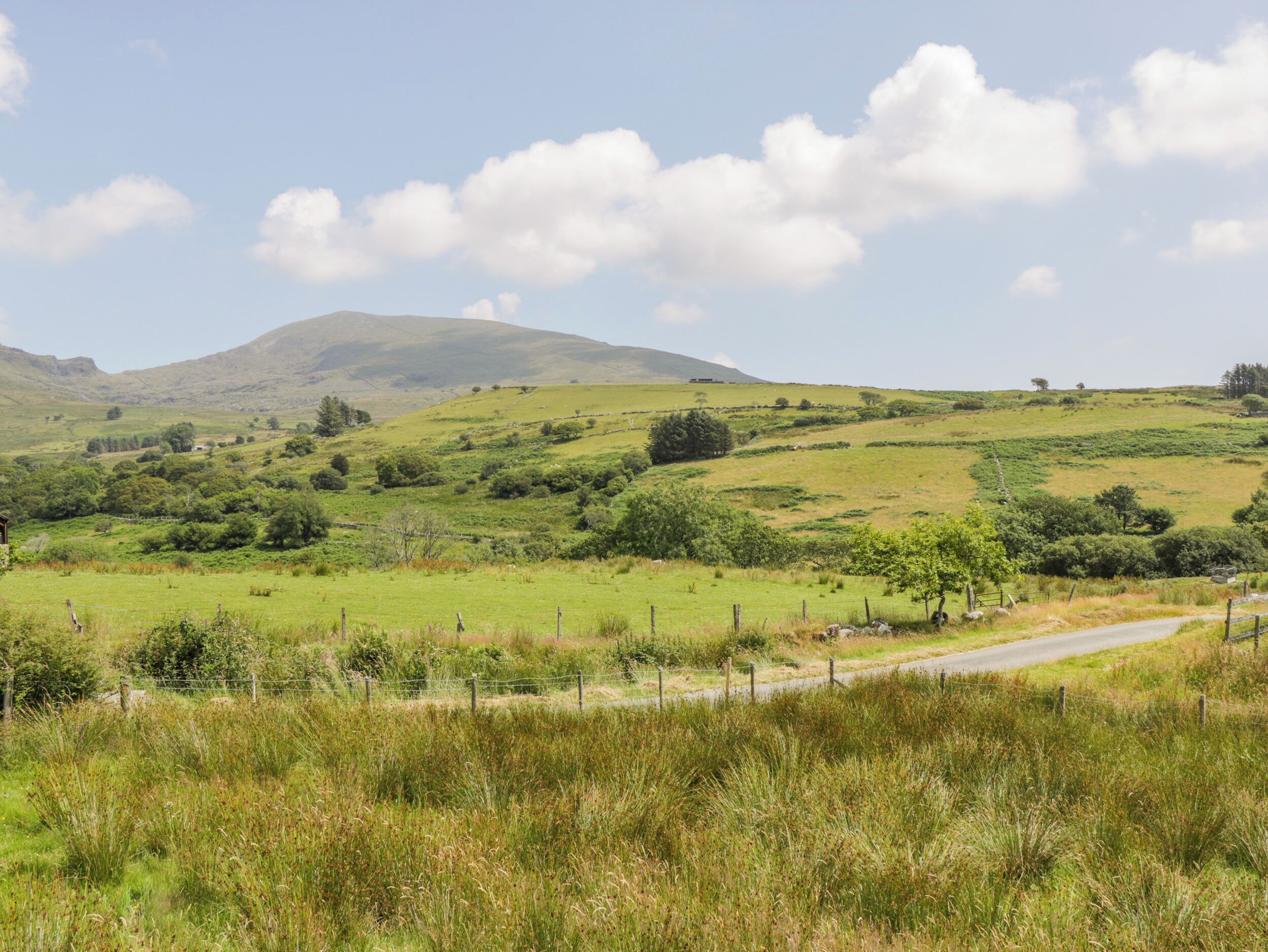 A rural landscape with rolling hills, a winding road, and a small building in the foreground.