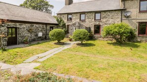 A stone building with a stone roof, a satellite dish, and a small garden with a pathway. - Melin Bach (Garndolbenmaen)