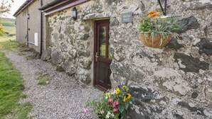 A stone building with a wooden door, a sign reading "Melin Bach", and a hanging flower basket. - Melin Bach (Garndolbenmaen)
