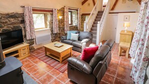 A cozy living room with a stone wall, wooden beams, a fireplace, a sofa, a TV, and a staircase. - Melin Bach (Garndolbenmaen)