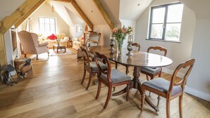 Amplio loft con techo alto, vigas de madera, zona de comedor con mesa y sillas redondas, un rincón de estar acogedor con sofás y ventanas grandes que dejan entrar luz natural.