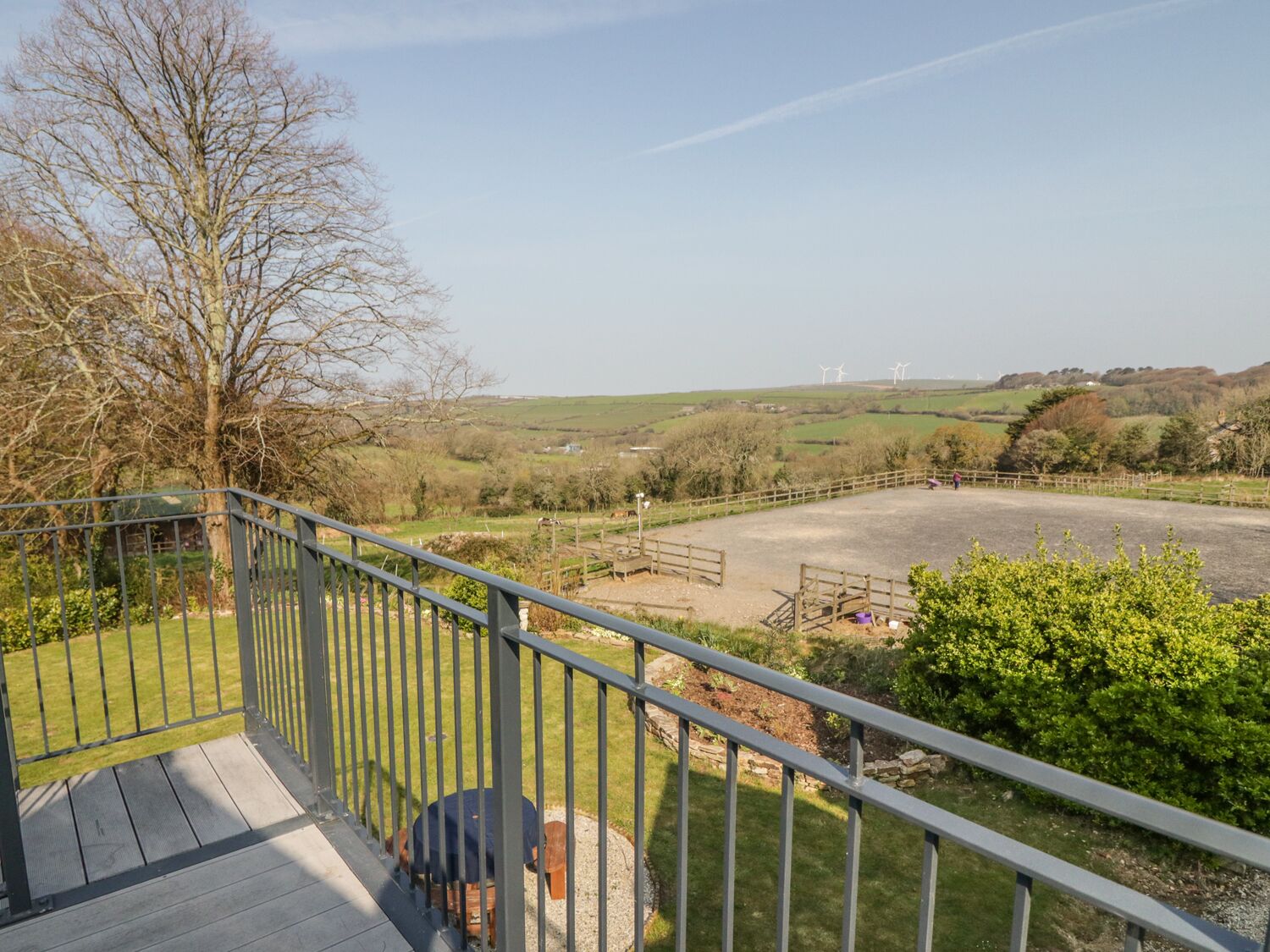 A balcony with a view of a fenced riding arena and wind turbines in the distance.