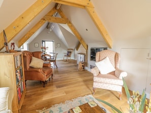 Um quarto de loft aconchegante com teto inclinado, vigas de madeira, piso de madeira, uma janela grande, uma cama, um aparador e uma cadeira.