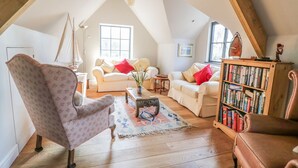 Una sala de estar estilo loft acogedora, con techo alto, vigas de madera, un ventanal grande, una estantería y un sillón con estampado.