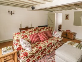 Una sala de estar acogedora con un sofá floral, un cofre de madera y una mesita con revistas.