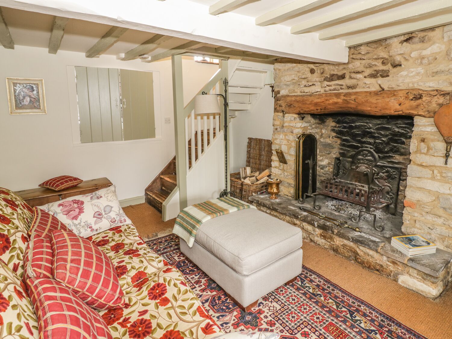 A cozy living room with a fireplace, a sofa with floral cushions, a staircase, and a rustic stone wall.