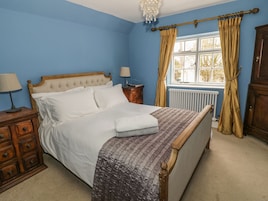 A bedroom with a bed, wooden nightstands, a dresser, a radiator, and a window with curtains.