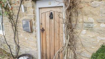 A stone cottage with a wooden door, a mailbox, and a sign indicating a fountain view.