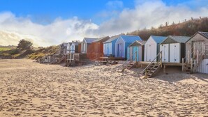 A row of beach huts with wooden stairs leading up to them, situated on a sandy beach with a clear sky. - Castell (Pwllheli)