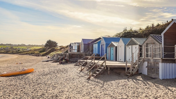 A row of beach huts with wooden stairs leading up to them, situated on a sandy beach. - Castell (Pwllheli)