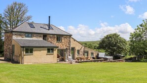 Una casa de piedra con techo inclinado, chimenea y un patio con muebles de exterior.