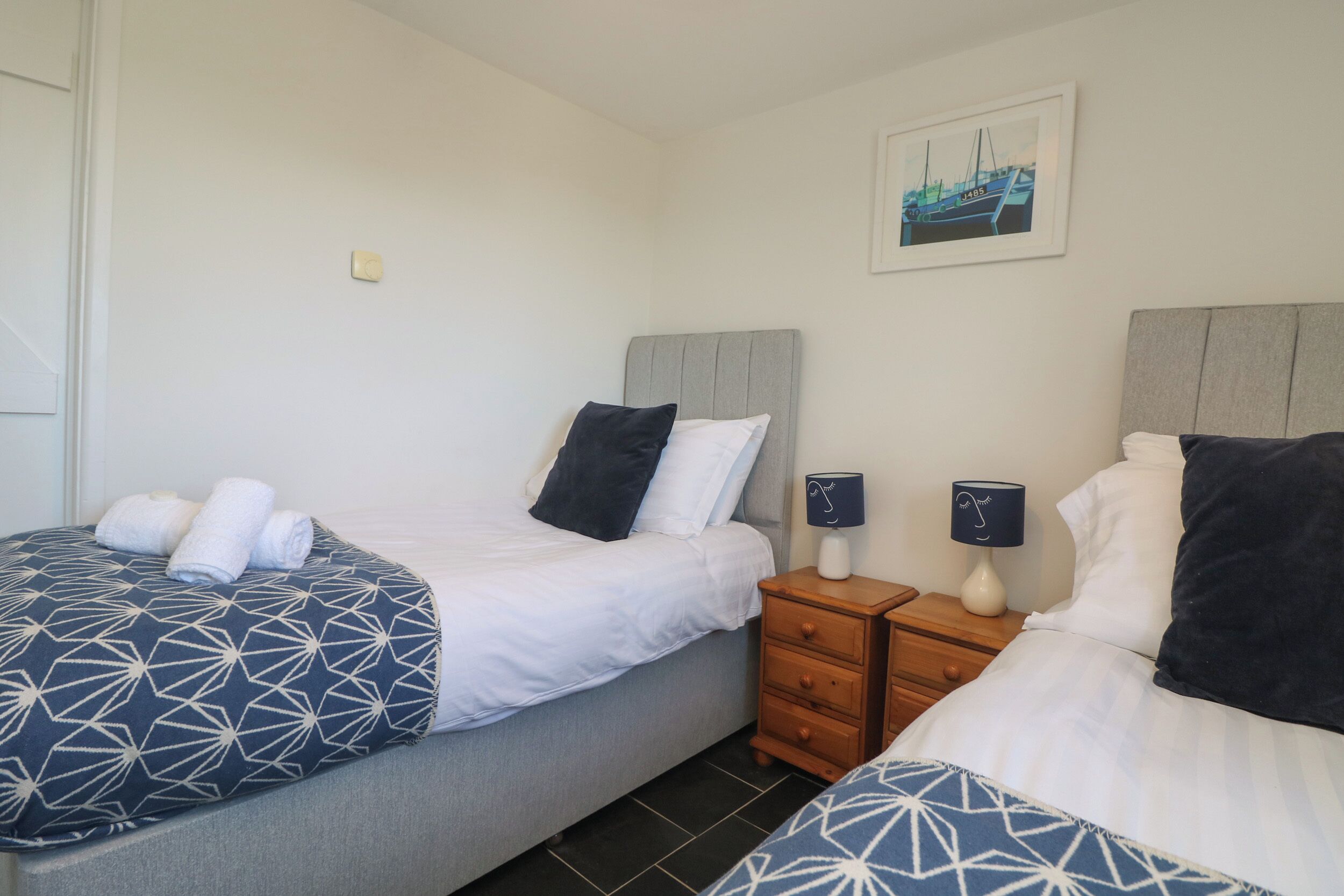 A hotel room with two beds, each with a patterned bedspread, a nightstand with a lamp, and a framed picture on the wall.