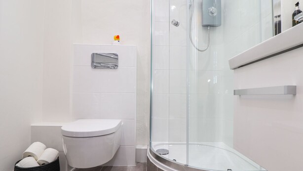 A modern bathroom with a glass-enclosed shower, a toilet, and a black basket with toilet paper.