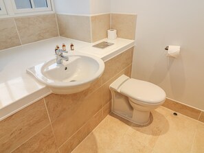 A bathroom with a white sink, a toilet, and beige tiles. - Frost (Ambleside)