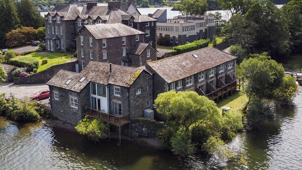 Un bâtiment en pierre doté de nombreuses fenêtres et d’un balcon, situé au bord d’une rivière.