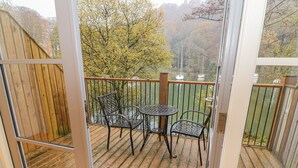 Une terrasse avec une table et des chaises, donnant sur une étendue d’eau et des arbres.