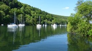 Un lac paisible où plusieurs voiliers sont amarrés près d’une rive bordée d’une forêt.
