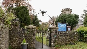 Un portón de piedra con un cartel que indica La Iglesia de San Leonardo Shipham, un muro de piedra y un poste de luz.