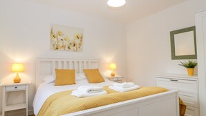 A neatly arranged bedroom with a bed, bedside tables, a nightstand, a dresser, and a mirror. - Stable Cottage (Winscombe)