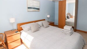 Un dormitorio con una cama grande, dos mesitas de noche, una silla, un espejo y un cuadro en la pared.
