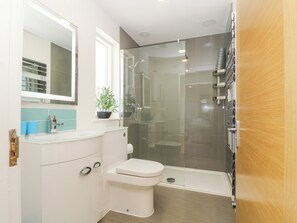Un baño moderno con ducha de vidrio, un inodoro blanco y un lavamanos con espejo.