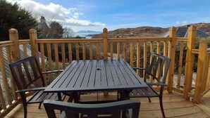 En träveranda med ett bord och stolar, med utsikt över ett vackert landskap med berg och en sjö eller ett annat vattendrag.