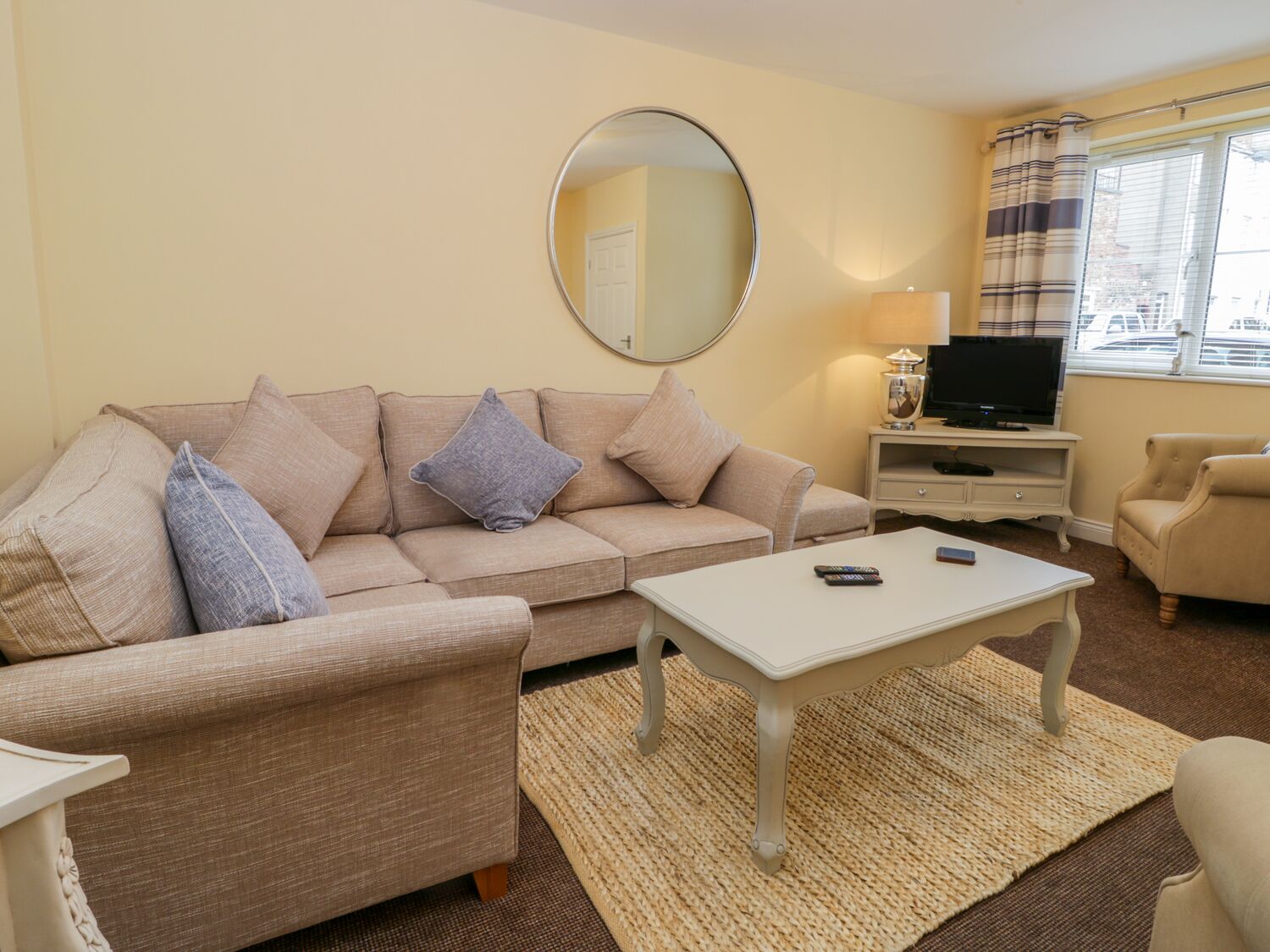 A living room with a sofa, armchair, coffee table, TV, and a mirror.