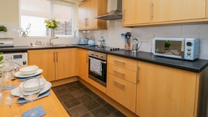 A modern kitchen with wooden cabinets, a black countertop, a built-in oven, a microwave, and a window with blinds. - Valiant House (Scarborough)
